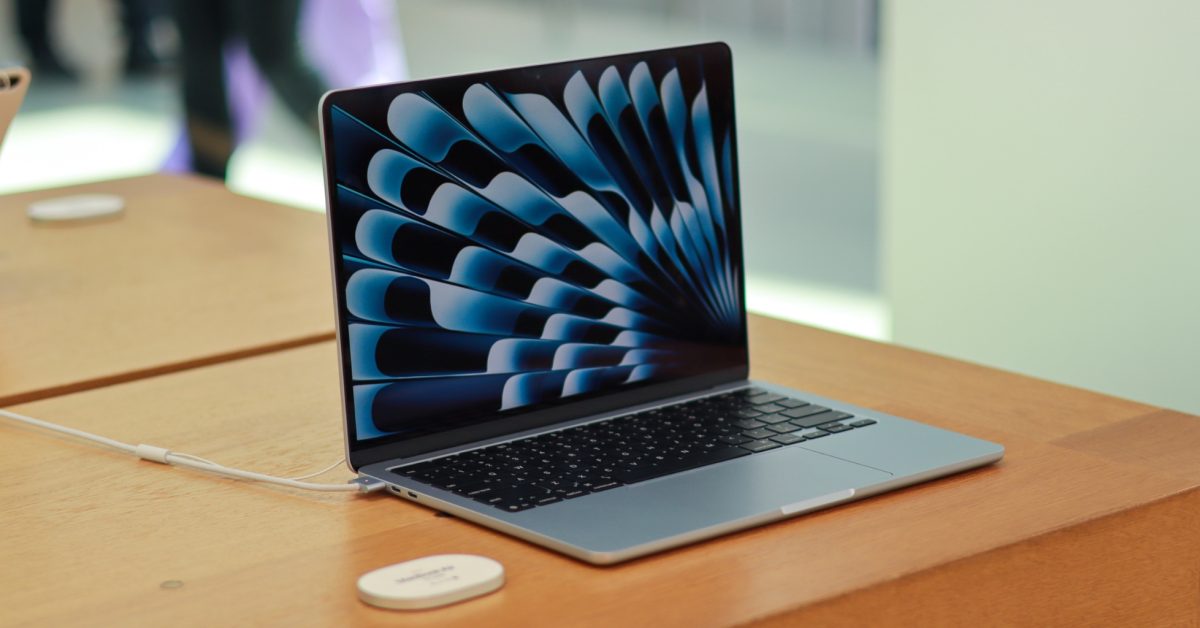 "Open laptop with a colorful abstract display on the screen, positioned on a wooden table. A white wireless charging pad is visible nearby."