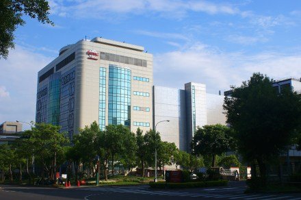 "Modern glass-fronted building surrounded by trees, with a clear blue sky in the background."