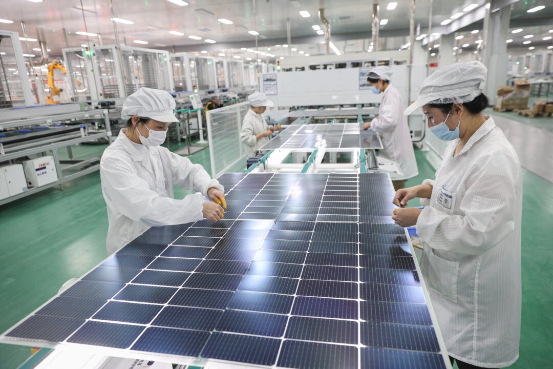 "Workers in white lab coats and masks assembling solar panels in a manufacturing facility with green flooring and various machinery in the background."