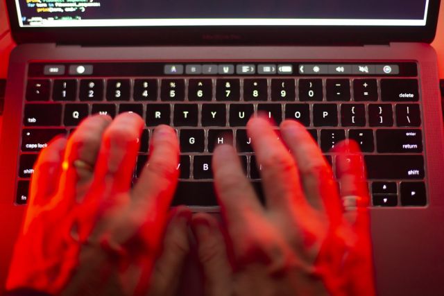 "Hands typing on a laptop keyboard illuminated with red lighting, with a partial view of the screen displaying code or text."