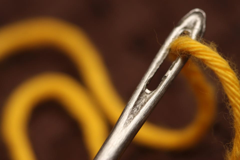 Close-up of a sewing needle threaded with yellow thread.