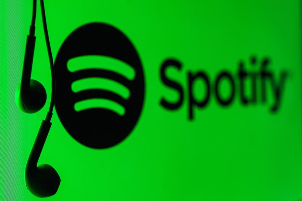 Black earbuds hanging in front of the Spotify logo and name on a bright green background.