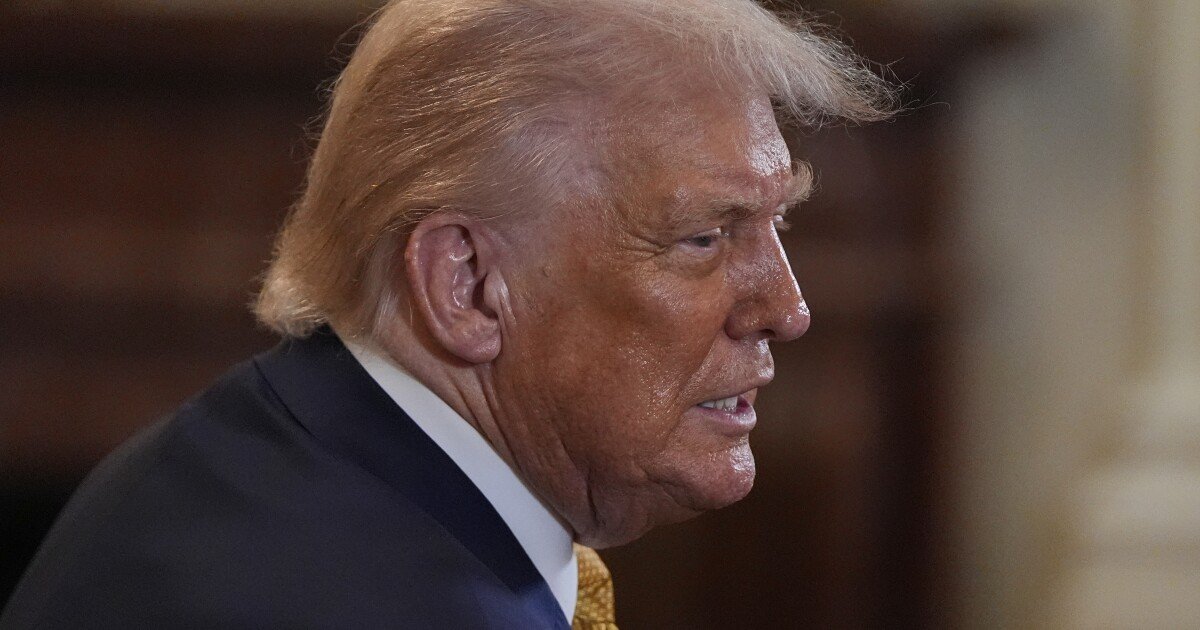 "Donald Trump in profile, facing right, with blond hair and a dark suit, appearing to speak."