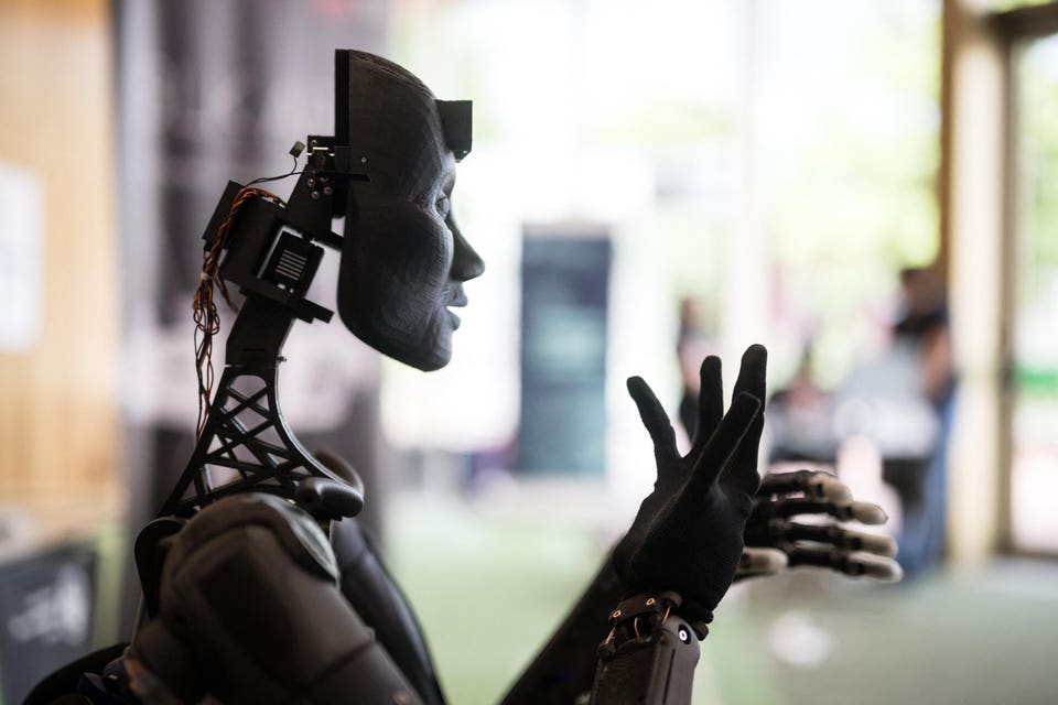 Dark robotic figure with a human-like profile and exposed mechanical components, extending a gloved hand.