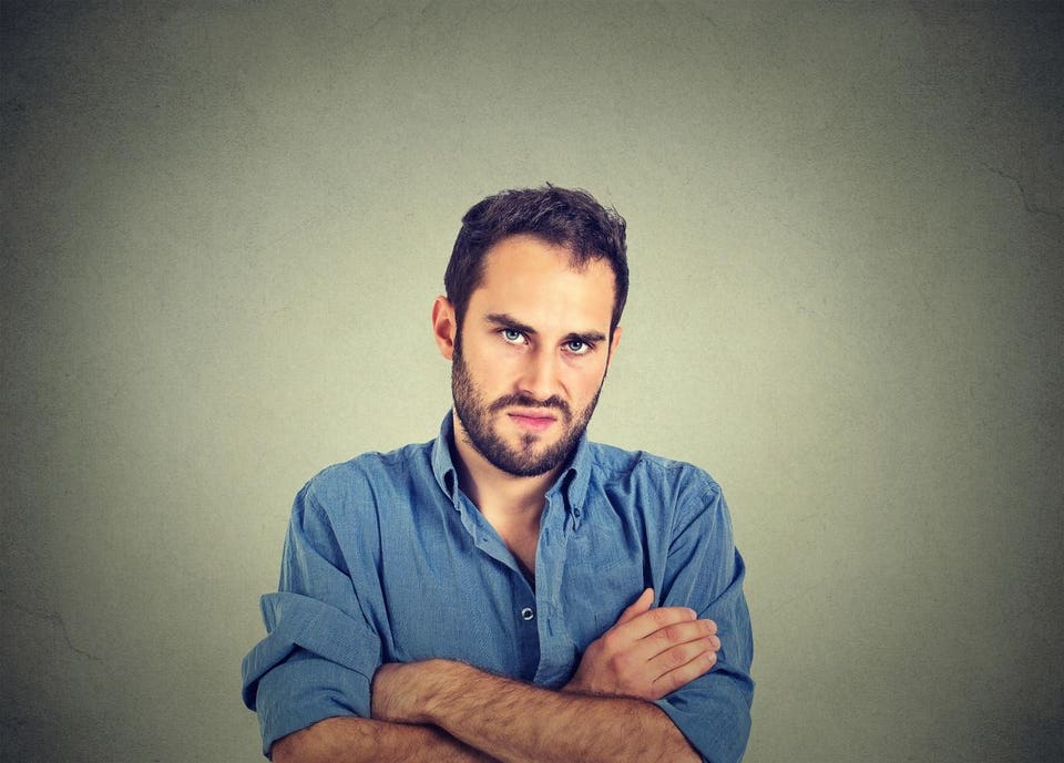 Man with a beard and blue shirt, arms crossed, with a stern expression.