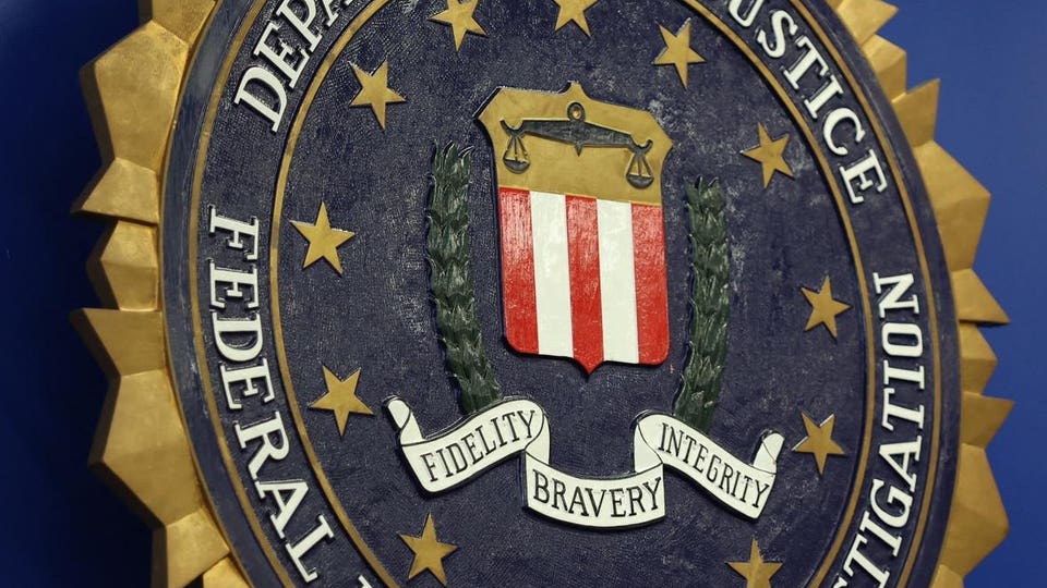 FBI seal, a dark blue circle with gold stars and "FEDERAL BUREAU OF INVESTIGATION" around a shield featuring red and white stripes, scales of justice, and a banner with "FIDELITY," "BRAVERY," "INTEGRITY."
