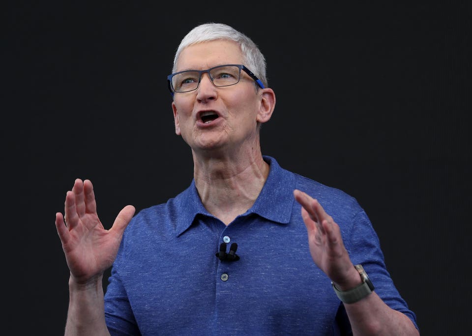 Tim Cook, CEO of Apple, speaking and gesturing, wearing a blue polo shirt and an Apple Watch.