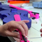 Hands holding a bright pink violin bow, with a purple violin body in the background.