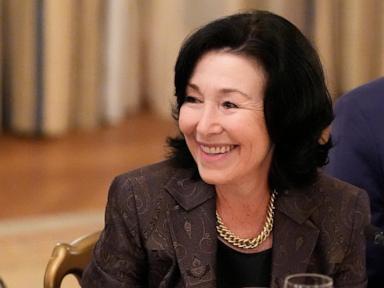 Smiling woman with dark hair, wearing a patterned blazer and gold chain necklace.