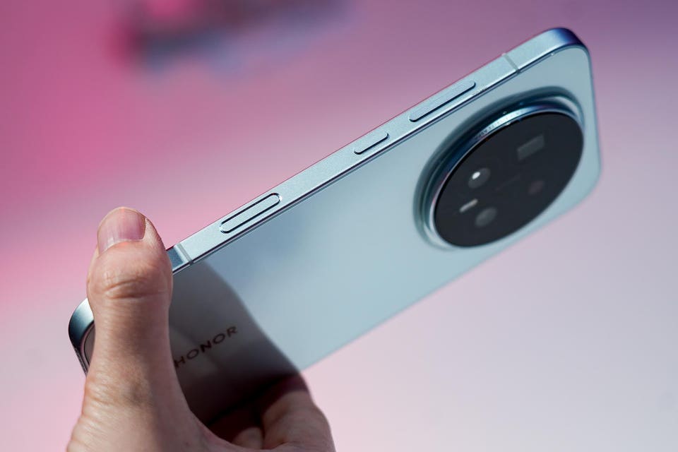 Hand holding a light blue Honor smartphone, showcasing its side buttons and large circular camera module on the back.