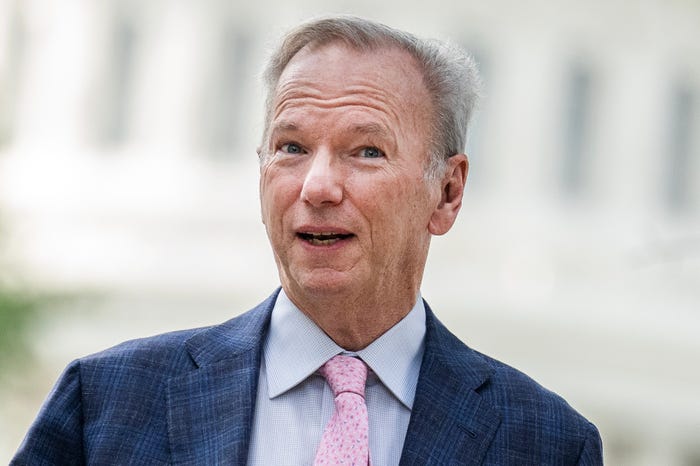 "Man with grey hair wearing a blue plaid suit, light blue shirt, and pink tie."