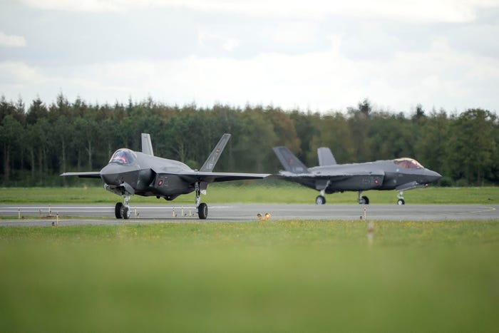 Two F-35 fighter jets on a runway with a forest in the background.