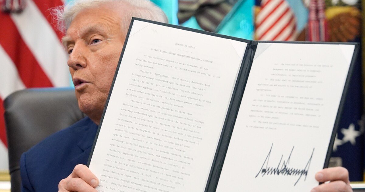 Donald Trump holds an Executive Order document titled 'Saving TikTok while Protecting National Security,' displaying his signature, with a US flag in the background.