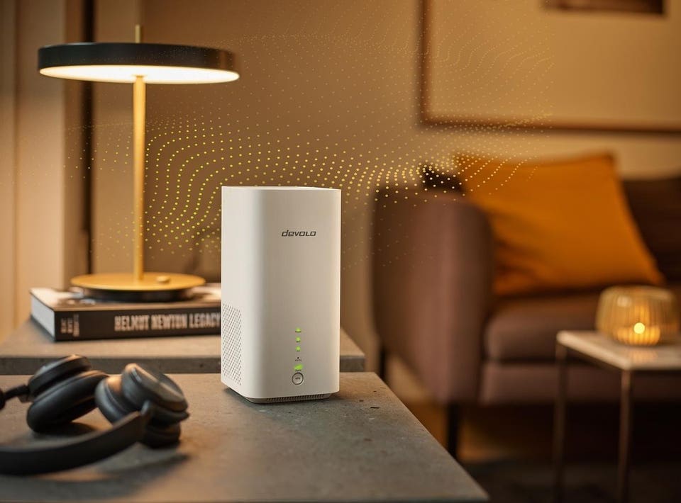 White Devolo network device emitting golden signal waves on a table, with headphones and a lamp in a modern living room.