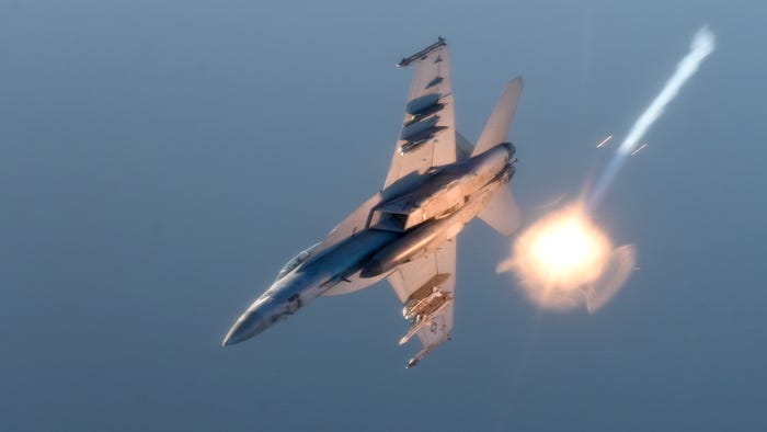 F/A-18 Super Hornet fighter jet deploying a bright flare against a blue sky.