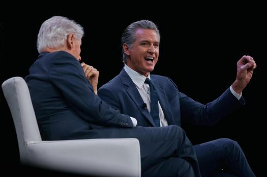 Former President Bill Clinton, seen from behind, listening to Governor Gavin Newsom, who is smiling and gesturing.