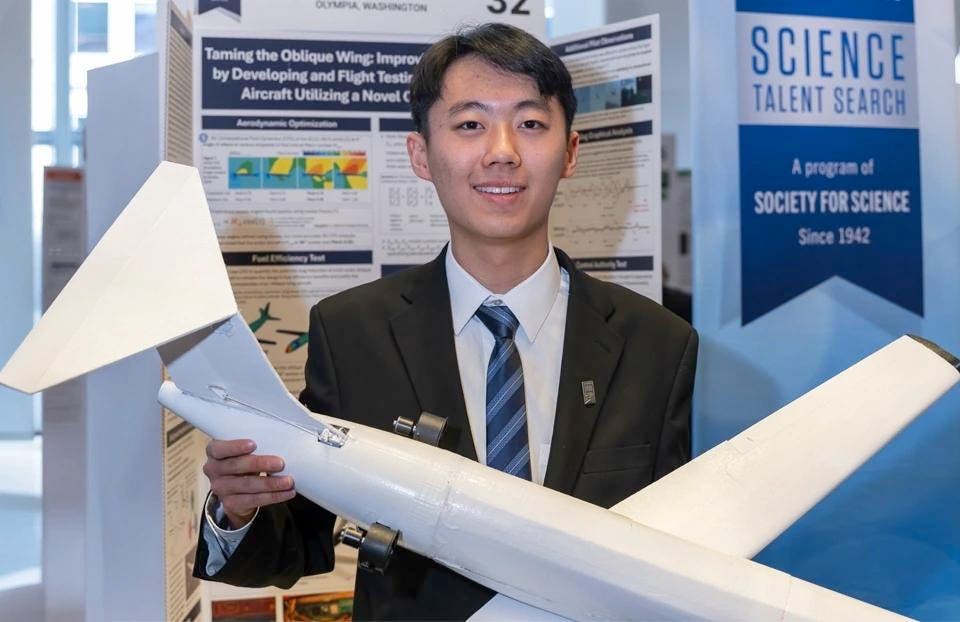 Smiling young man in a suit holds a white model airplane in front of a project poster titled "Taming the Oblique Wing" and a "Science Talent Search" banner.