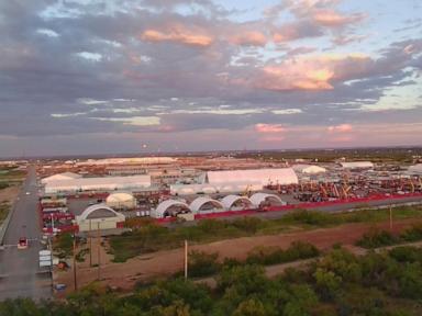 Aerial view of a large temporary facility with numerous white tents and industrial equipment under a dramatic cloudy sky.