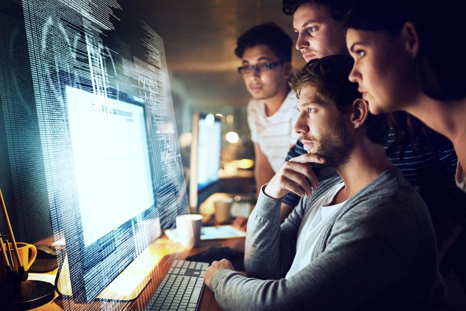 Team of four colleagues intently examining a computer screen displaying an overlay of digital code.