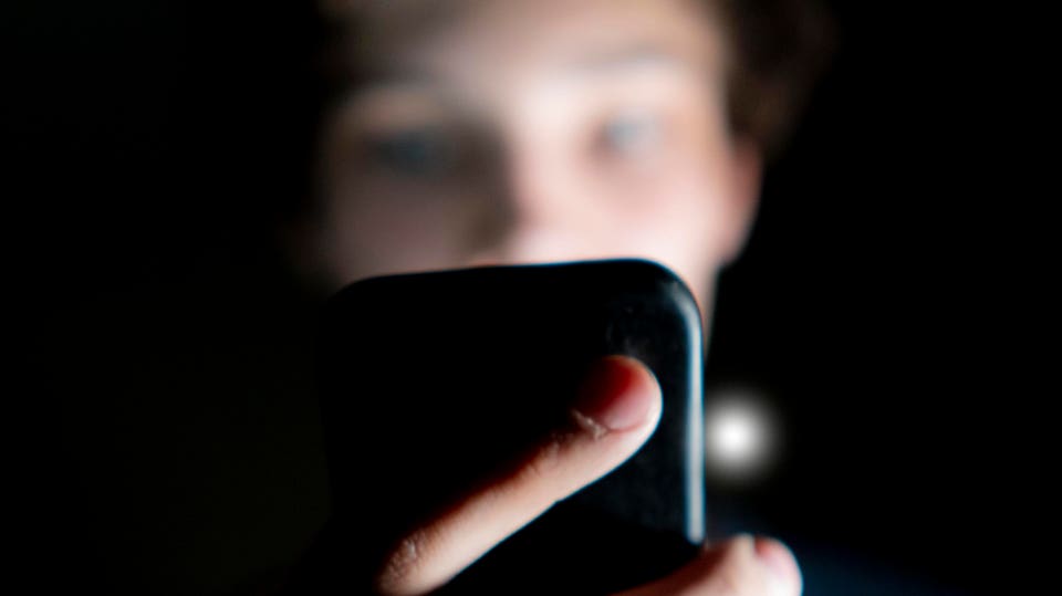 Person's face illuminated by a smartphone screen in a dark room.