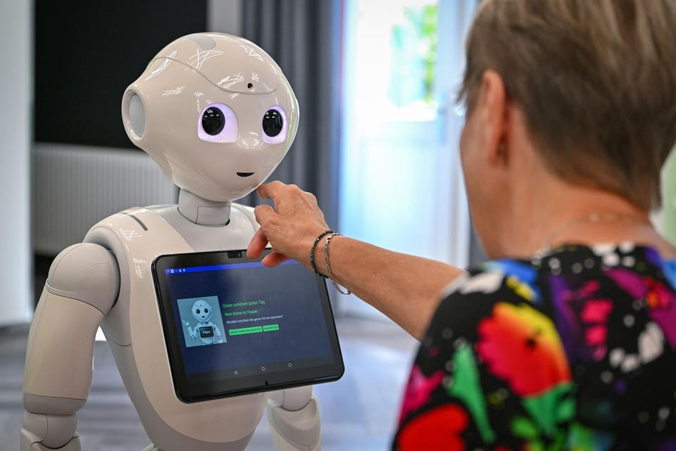 A person's hand touches the head of a white Pepper robot, which displays "My name is Pepper" on its chest screen.