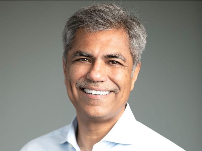 Smiling man with grey hair and a mustache wearing a collared shirt.