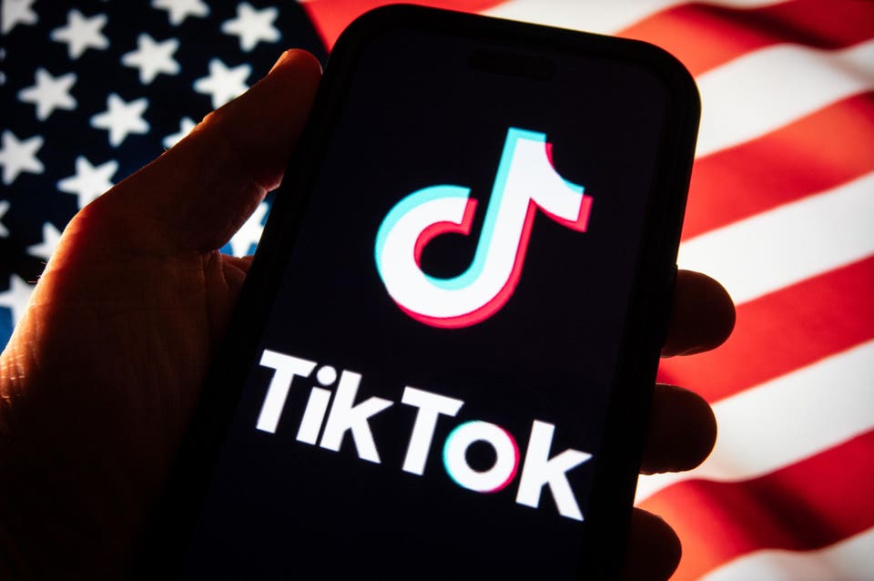 "Smartphone displaying the TikTok logo, held against a blurred American flag."