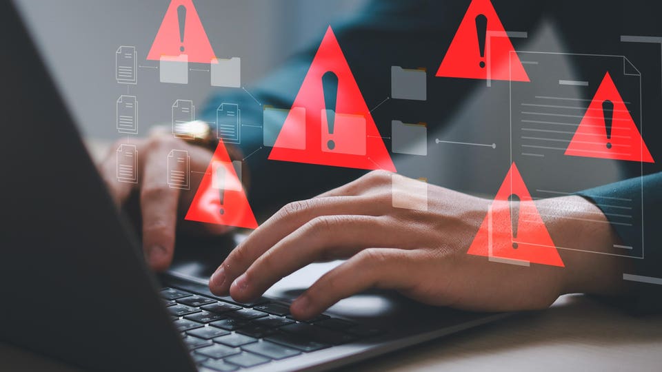 Hands typing on a laptop keyboard, surrounded by digitally overlaid red warning triangles and document icons, suggesting data security risks or system errors.