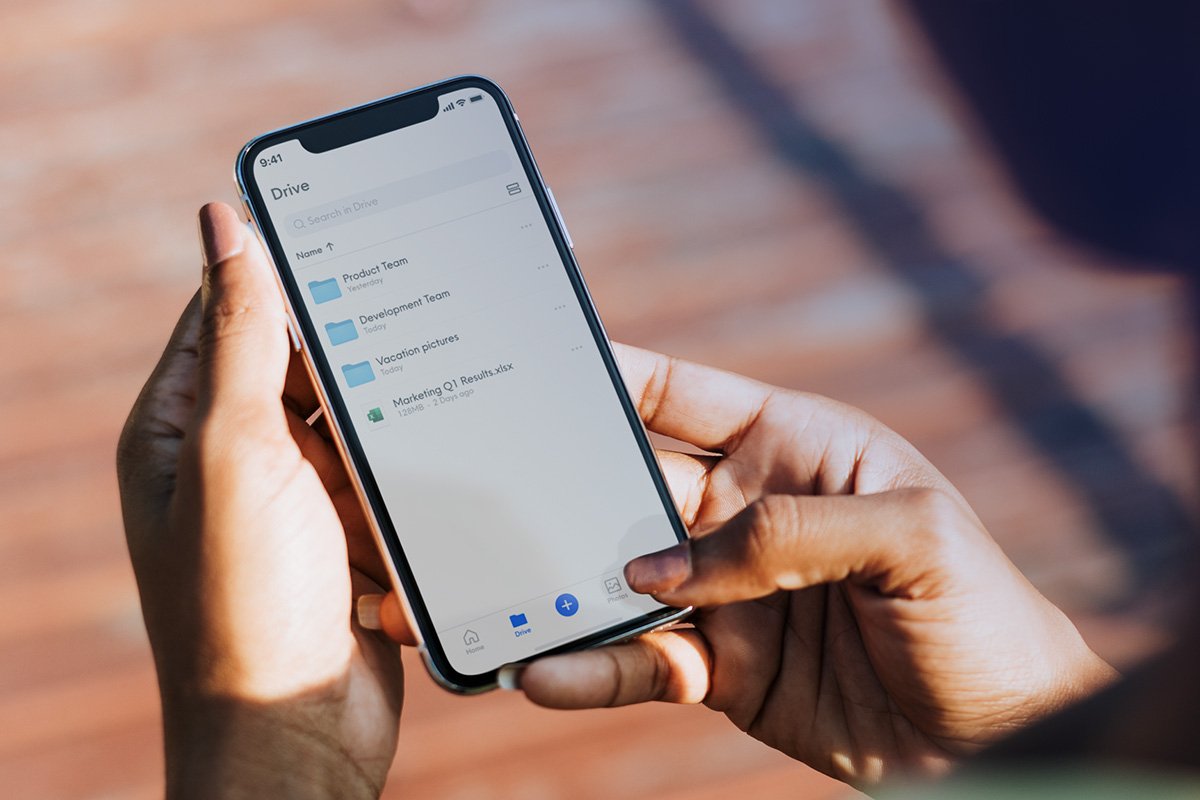 Hands holding a smartphone displaying the Drive app with folders and files.