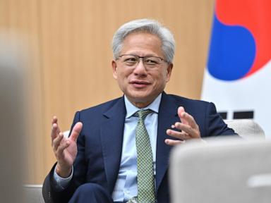 Man in a dark suit, light blue shirt, and patterned green tie speaking, with the South Korean flag visible in the background.