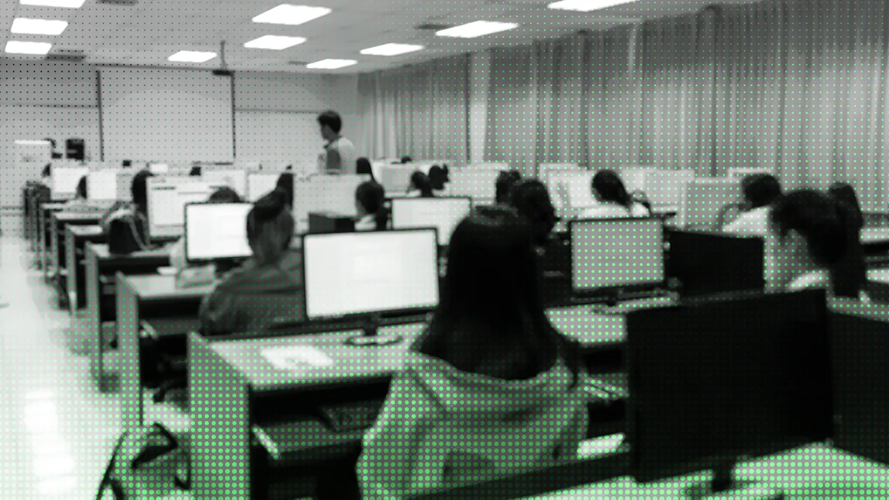 A large room with rows of people seated at individual computer workstations.