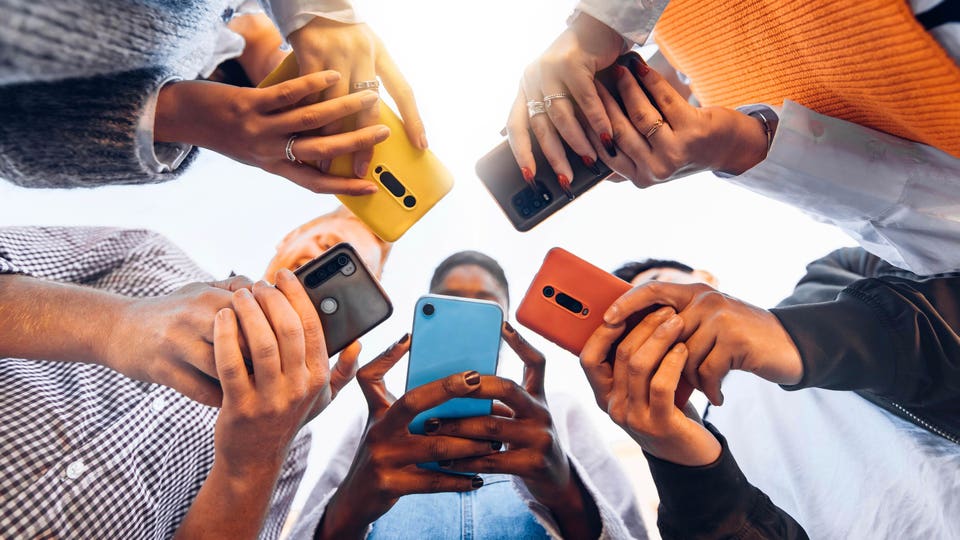 Low-angle view of multiple hands holding smartphones with colorful cases in a circle.