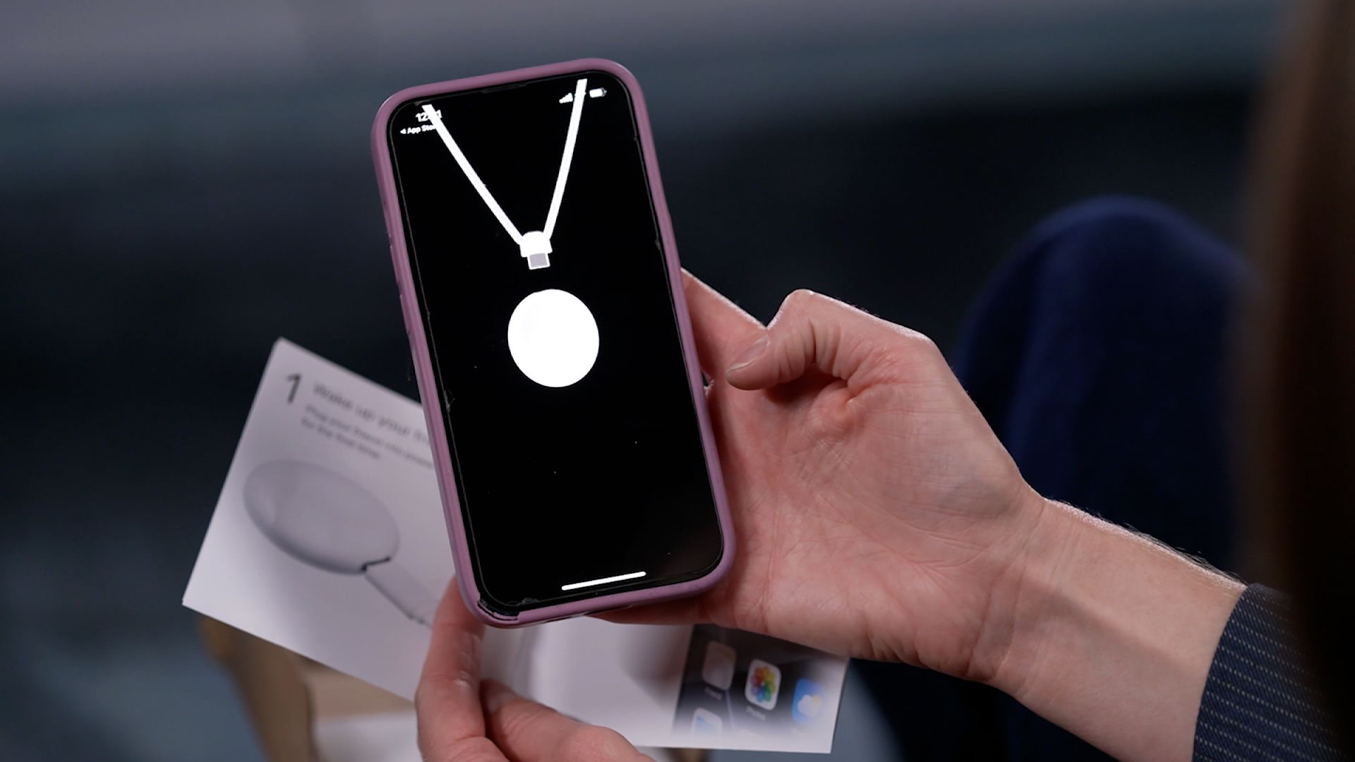 Hands hold a smartphone displaying a device pairing interface with a large white circle, alongside instructions showing a white circular tracker.